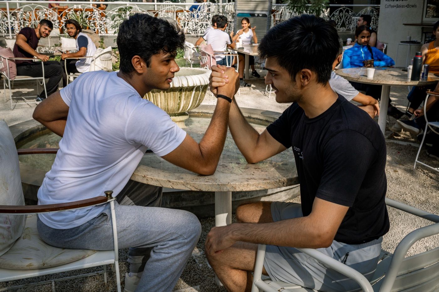 Two friends arm-wrestling and laughing at a café table after a Sunday morning run