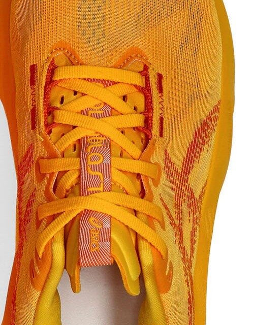 Macro shot of the ASICS Novablast 5's engineered mesh upper in the all-orange Yamabuki/Anzu colourway, showing the laces and tongue