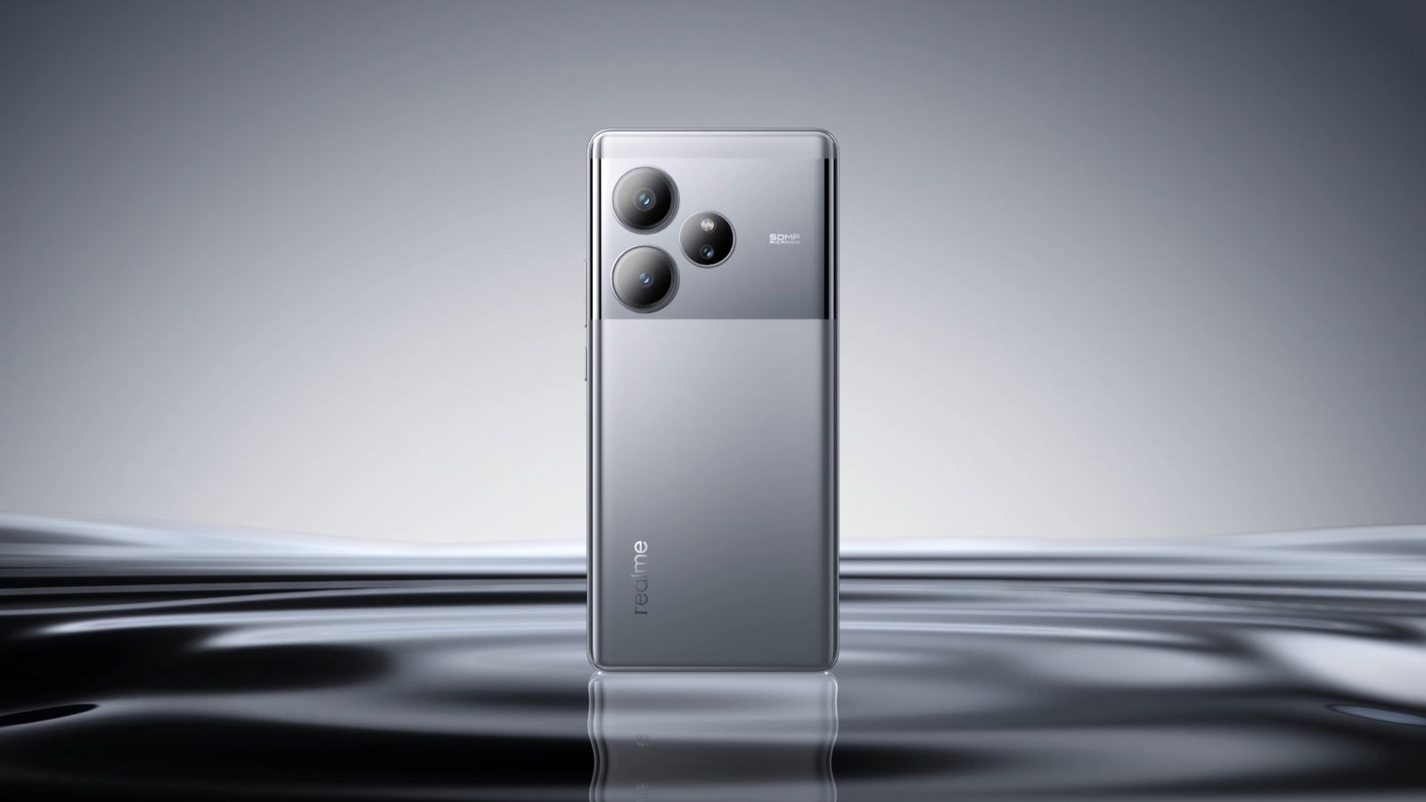 realme GT 6 in Fluid Silver, back panel and triple camera module, standing upright on a reflective studio surface